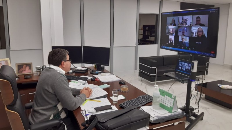 Defensor Público-Geral, Antônio Flávio de Oliveira, sentado em sua mesa, observando a videoconferência no televisor.