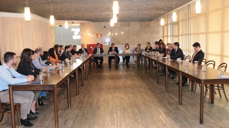 mesa de reuniões, em formato de U, com todos sentados no seu entorno