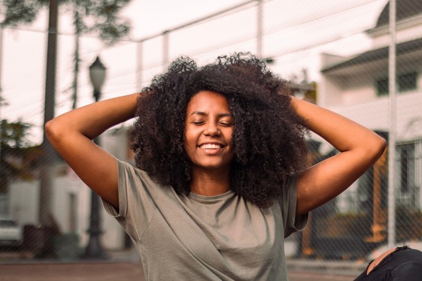 mulher preta sorrindo com as mãos nos cabelos