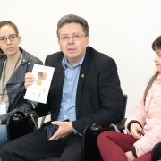 foto do defensor geral segurando uma cartilha. A sua esquerda, está sentada a coordenadora dos estágios e, a sua direita, dois participantes da reunião