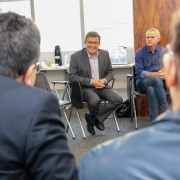 em primeiro plano, dois participantes de costas e desfocados enquanto que, no segundo plano, o presidente da AFAD está de frente para eles, sorrindo