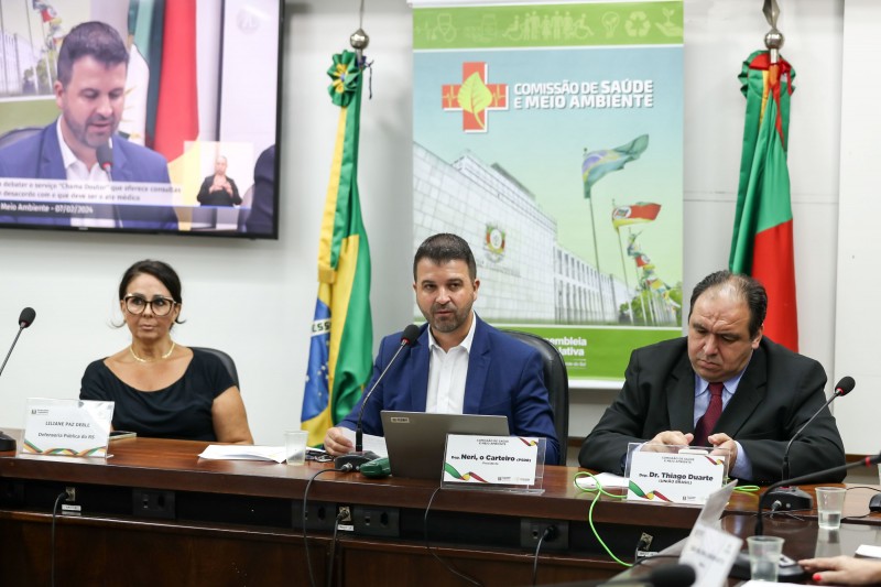foto de 3 integrantes da audiência, estão em uma mesa. entre eles a defensora e dois deputados