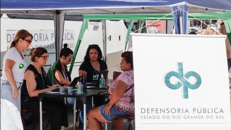 banner da defensoria e equipe trabalhando ao fundo