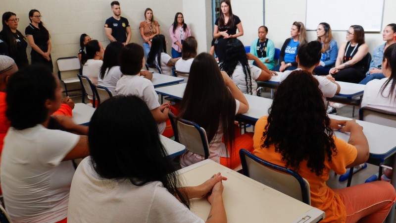 Mulheres presas assistem à aula. Ao fundo, professoras e representantes das instituições.