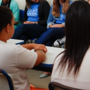 "Escola de Negócios" aparece em camiseta azul ao fundo.