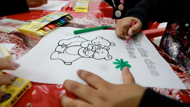 Criança em abrigo colore desenho com a frase "Feliz dia das Mães".
