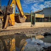 Escavadeira em frente à creche, há poças de água e barro no chão.