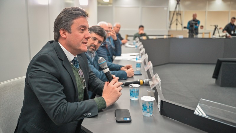 foto do defensor público renato munoz de oliveira santos, falando para um grupo sentado em uma mesa oval