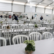Refeitório do CHA. Na imagem, há dezenas de mesas e cadeiras de plático. Em cima das mesas, há vasos de flores