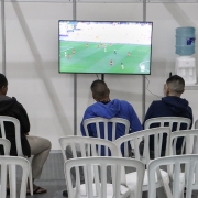 Pessoas que estão acolhidas assistem a jogo de futebol na televisão