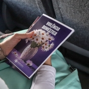 Mulher sentada em ônibus segura a cartilha da Defensoria. Lê-se "Violência Doméstica"