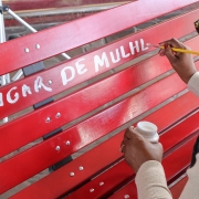 Mulher escreve em banco vermelho com tinta branca. Lê-se: "lugar de mulher".