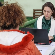 Em primeiro plano, uma mulher de costas está virada para outra que, em segundo plano, mexe em um computador.