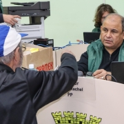 Em primeiro plano, um homem, de costas, conversa e gesticula com outro que, em segundo plano e de frente, aparenta ouvir.