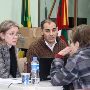 Uma mulher, de costas, está virada para outra mulher e um homem, que olham diretamente para ela.