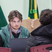 Uma mulher, de costas e sentada em uma cadeira, está virada para um homem que, de frente, olha diretamente para ela. 