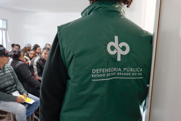 Servidor em primeiro plano, ao fundo público espera por atendimento.