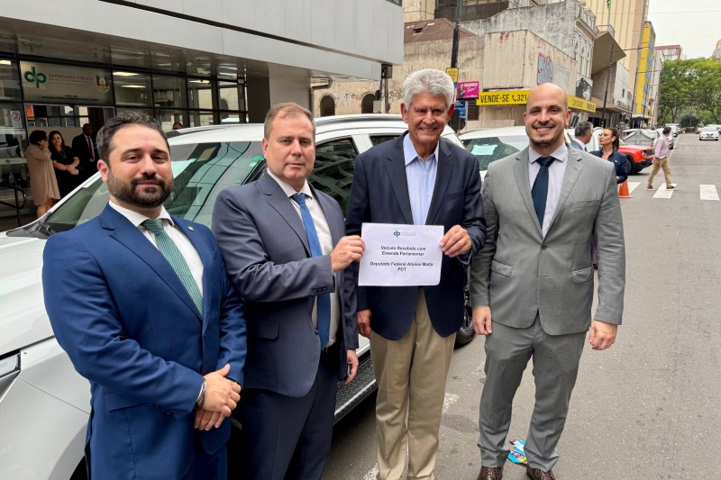 4 homens em frente a um carro na rua, todos de pé e um do lado do outro, posando para a foto. Os 2 do meio seguram um papel escrito "veículo recebido com emenda parlamentar" e "deputado federal afonso motta - PDT"