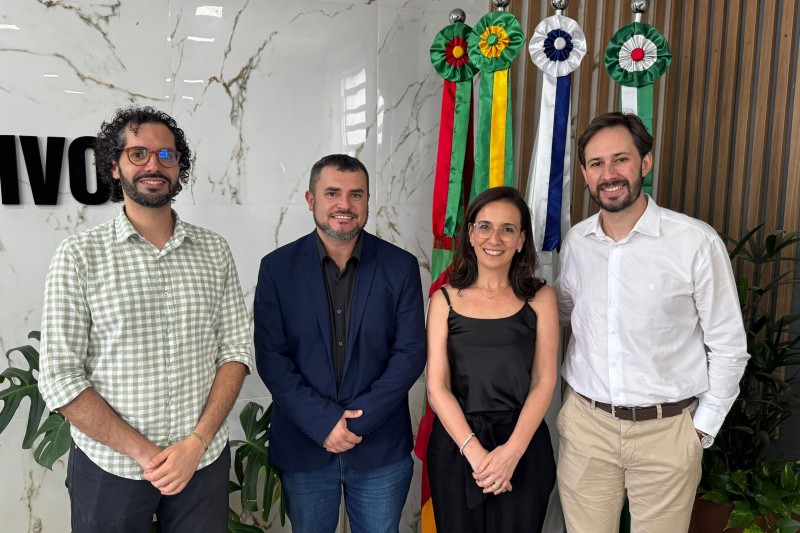 4 pessoas, 3 homens e uma mulher, de pé, posando para a foto em uma sala moderna.