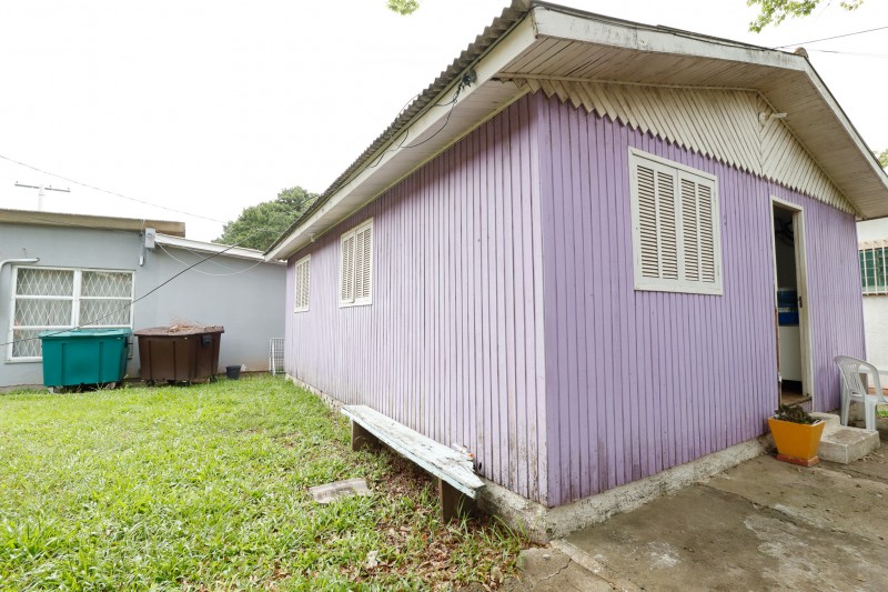 imagem da fachada da casa, que é de madeira, com uma porta e três janelas, na cor roxa