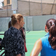 Crianças jogam bola ao fundo. Mulheres vistoriam a quadra.