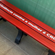 Um banco vermelho, onde se lê: "violência contra a mulher é CRIME!"