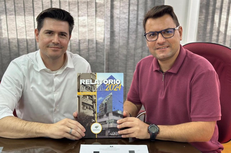 Na foto, vemos o o defensor público Rafael Bettio da Fonseca entregando uma cópia do último Relatório Anual ao prefeito, Luís Henrique Kittel.