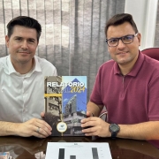Na foto, vemos o o defensor público Rafael Bettio da Fonseca entregando uma cópia do último Relatório Anual ao prefeito, Luís Henrique Kittel.