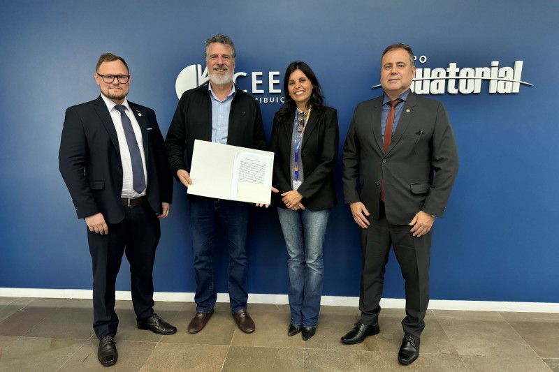 Defensor público-geral e representantes da CEEE posando para foto com termo de cooperação assinado.