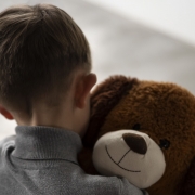Criança de costas segurando um urso de pelúcia