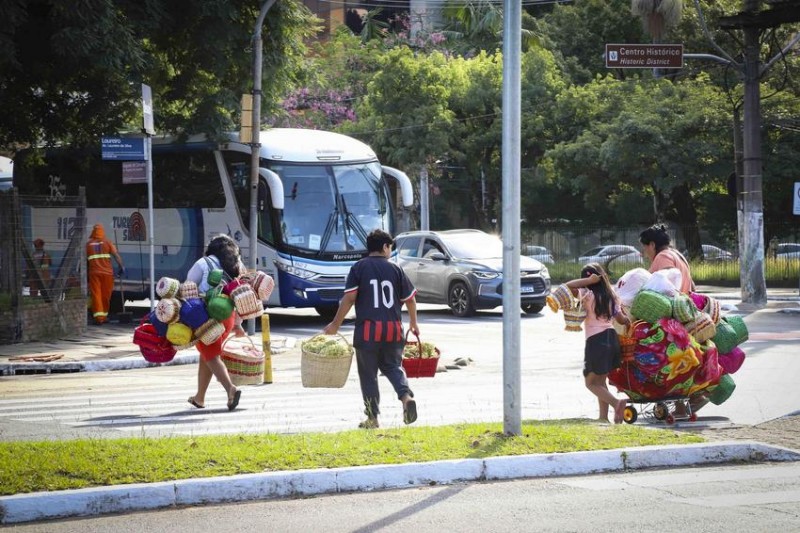Fam&iacute;lia ind&iacute;gena carrega cestas e artesanatos em rua de Porto Alegre.