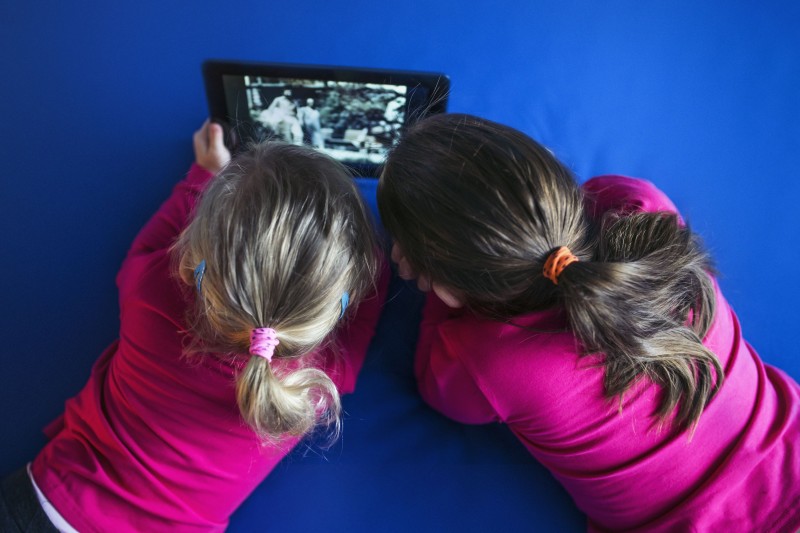 Imagem de duas crian&ccedil;as de costas, vestindo blusa rosa, segurando um tablet