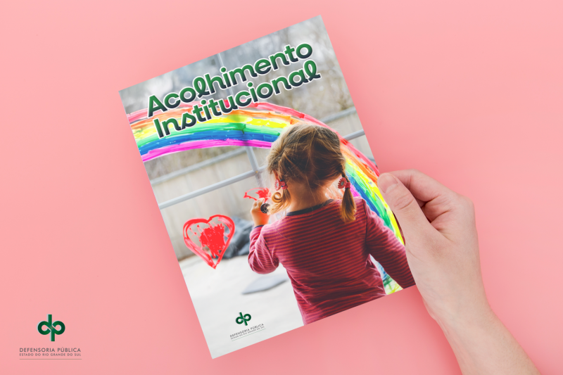 A imagem mostra a capa da cartilha em um fundo rosa. Na capa da cartilha, aparece a imagem de uma crian&ccedil;a de costas, em frente ao desenho de um cora&ccedil;&atilde;o e de um arco-&iacute;ris, abaixo de um texto onde &eacute; poss&iacute;vel ler "Acolhimento institucional".
