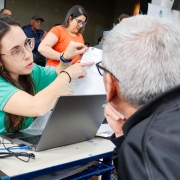 foto de uma servidora, de frente, apontando para um documento e mostrando para um senhor que está de costas para a foto