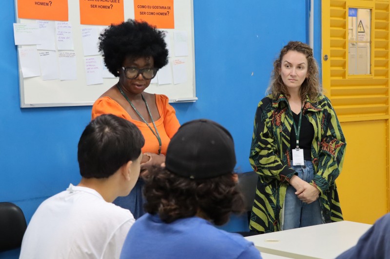 Duas psic&oacute;logas da DPE em p&eacute; dentro de uma sala de aula falando com internos da FASE