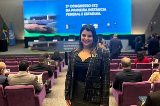 A imagem mostra a defensora p&uacute;blica Bibiana Ver&iacute;ssimo Bernardes em frente a uma tela com o nome do evento, intitulado "1&ordm; Congresso STJ da primeira inst&acirc;ncia federal e estadual".