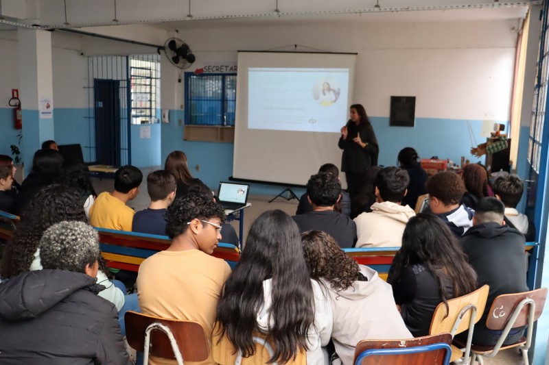 A imagem mostra os alunos da escola reunidos em um semic&iacute;rculo para assistir a palestra.