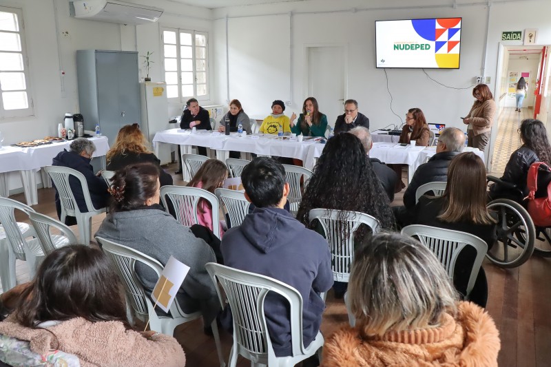 uma plateia com aproximadamente 15 pessoas est&aacute; assistido aos palestrantes 